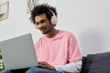 Şık bir genç adam, modern bir odada odaklanmış ve rahatlamış bir şekilde dizüstü bilgisayarla vakit geçirmekten hoşlanır..