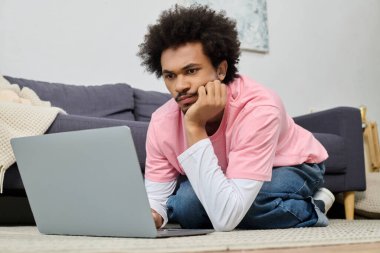 Yakışıklı genç bir adam yerde yatıyor, rahat bir yerde dizüstü bilgisayarına odaklanmış..