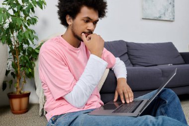 Odaklanmış adam rahat bir oturma odasında yerde dinlenirken dizüstü bilgisayarıyla çok meşgul oluyor.