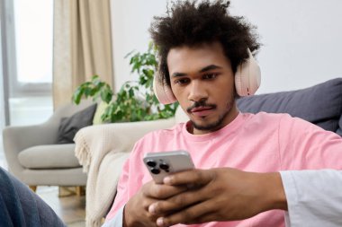 Kulaklıklı genç yakışıklı bir adam rahat rahat oturup rahat bir odada telefonuna bakıyor..