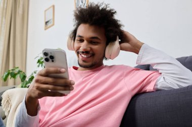 Yakışıklı genç adam akıllı telefonuyla müzik dinlerken gülümser, neşeli bir atmosfer yaratır..
