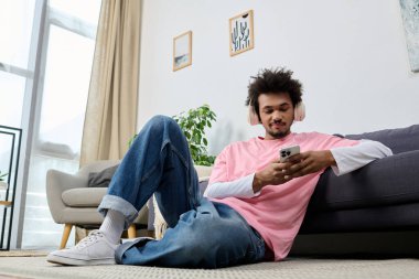 Yakışıklı bir genç adam yerde rahat bir şekilde uzanıyor, telefonu ve müziğine dalmış..