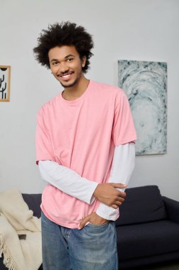 Kıvırcık saçlı neşeli genç adam rahat bir ortamda pozlar veriyor, pozitif enerji ve sıcaklık yayıyor..