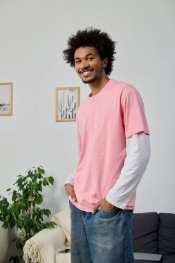 Pembe gömlekli yakışıklı genç bir adam evde eğlenirken kendine güvenerek gülümsüyor..