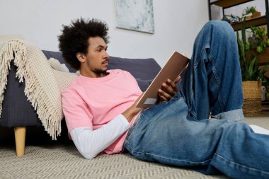 Pembe gömlekli genç bir adam yerde rahatça uzanıyor, dikkatle okuyor..