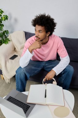 Gündelik kıyafetli genç adam evde dizüstü bilgisayar ve defterle çevriliyken fikir alışverişinde bulunuyor..