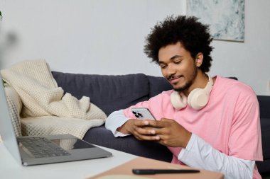 Akıllı telefonuyla meşgul yakışıklı genç bir adam rahat bir yerde oturuyor..