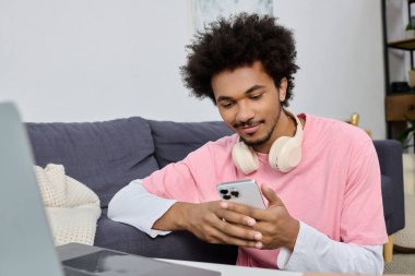 Genç, yakışıklı bir adam evinde rahat rahat otururken akıllı telefonuna bakıp gülümsüyor..