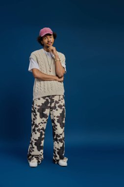 Şık bir genç adam cesur görünmek için kendine güvenen bir süveter ve desenli pantolon giyiyor..