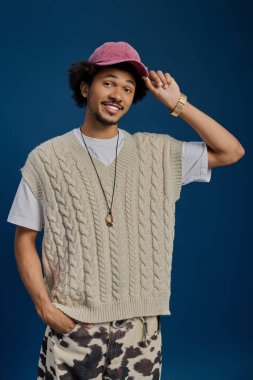 Neşeli genç adam sevimli kişiliğini ve modasını sergileyen rahat bir kazak ve şapka giyiyor..