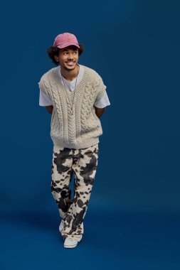 Genç ve yakışıklı bir adam, rahat örülmüş bir yelek ve eşsiz bir pantolon giyerken cazibesini sergiler..