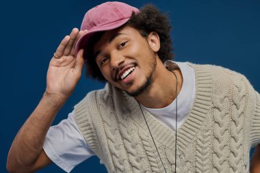 Çekici genç adam neşeyle gülümsüyor, eşsiz tarzını mavi bir zemine karşı sergiliyor..