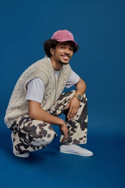 Çekici genç adam, modaya uygun giysiler içinde, rahat bir stil ve kişilik yayarak çömeliyor..