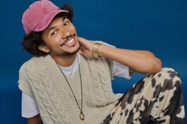 Rahat bir genç adam rahat bir süveter ve şapka giyiyor neşeli bir sahnede neşeli kişilikler sergiliyor.