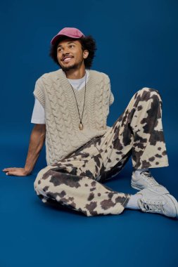 Genç yakışıklı bir adam rahat bir şekilde yerde oturuyor, şık bir kıyafet giyiyor, sıcak bir şekilde gülümsüyor..