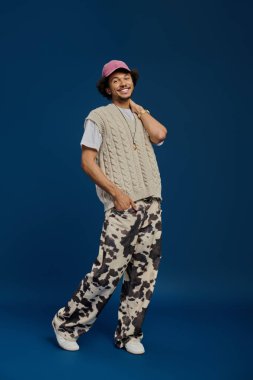 Genç bir adam modaya uygun bir kıyafet giyerek çekiciliğini sergiliyor. Maviye karşı güvenle poz veriyor..