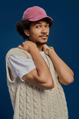 Genç ve çekici bir adam moda anlayışını rahat bir yelek ve şapkayla sergiliyor..