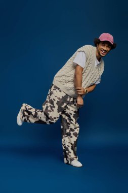 Genç ve yakışıklı bir adam tek ayak üstünde, şık kıyafetlerini ve parlak gülümsemesini sergiliyor..