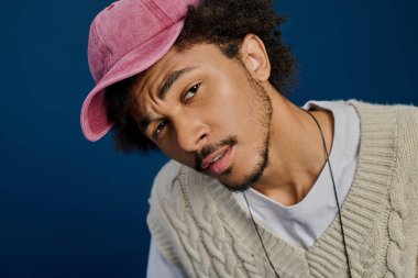 Şık bir genç adam mavi arka planda şakacı poz verir..