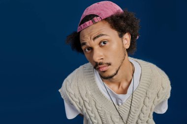 Şık, kıvırcık saçlı ve şapkalı genç bir adam kendine has modasını cesur bir şekilde sergiliyor..