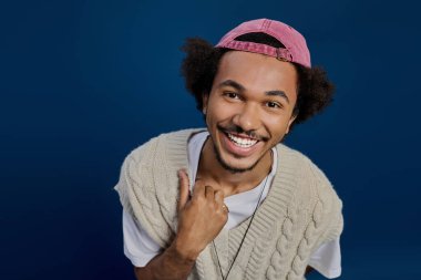 Neşeli genç bir adam şık bir şapka ve süveter giyerken parlak bir gülümsemeyle kendine güvenir..