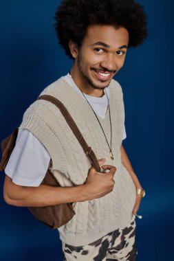 Hoş bir süveter ve modaya uygun pantolon giyen yakışıklı genç adam gülümsemesini ve tarzını gösteriyor..