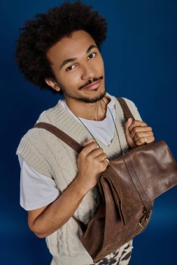 Çekici bir gülümsemesi olan genç bir adam, modaya uygun kıyafetlerini ve aksesuarlarını sergiliyor..