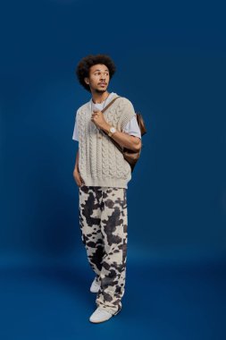 Genç, yakışıklı bir adam, şık bir süveter ve eşsiz bir pantolon giyer. Aynı zamanda şık ve çekici bir poz verir..