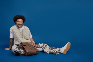 Çekici bir genç adam, parlak mavi bir arka plana karşı modaya uygun giysiler içinde rahatlar..