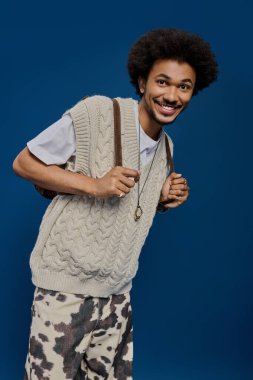 Rahat süveter ve desenli pantolon giyen neşeli genç adam sahneye pozitif enerji getiriyor..