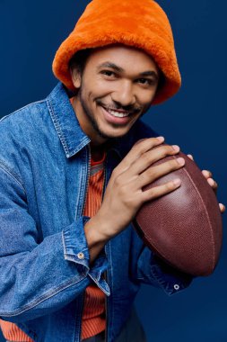 Şık bir genç adam elinde futbol topu tutarken, neşeli bir ruh sergileyerek ışıl ışıl gülümser..