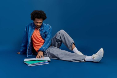 Yakışıklı genç adam rahat bir şekilde yerde oturuyor, etrafındaki defterlerle ders çalışıyor..