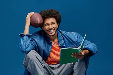 Yakışıklı genç adam elinde futbol topu tutarken, kitap okurken ve mutluluğu gösterirken rahatlıyor..