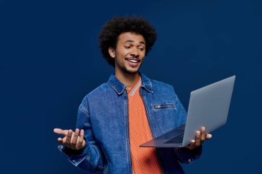 Neşeli genç bir adam dizüstü bilgisayarıyla etkileşime geçiyor, nefes kesici mavi bir ortamda heyecanını paylaşıyor..