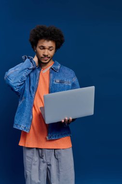 Afro saçlı genç bir adam özenle dizüstü bilgisayar tutuyor, şık bir kıyafet giymiş..