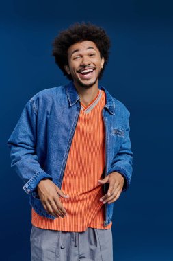 Kıvırcık saçlı neşeli bir genç adam renkli bir kıyafet giyerken mutluluğunu ifade eder..