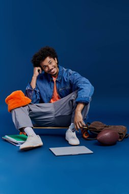 Yakışıklı genç bir adam renkli çalışma eşyalarıyla çevrili bir kaykayın üzerinde dinleniyor..