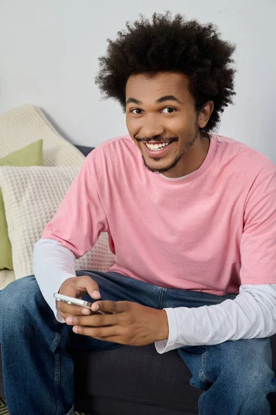 Neşeli bir oturma odasında akıllı telefonuyla meşgul olan parlak bir gülümsemesi olan genç adam..