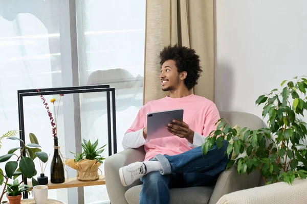 Genç bir adam yeşilliğin ortasında tabletini kullanarak şık bir sandalyede dinleniyor..