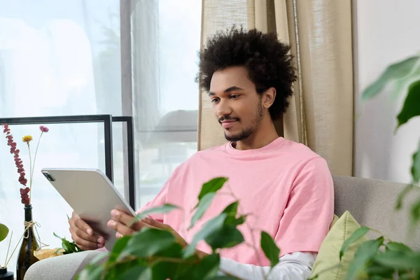 Genç yakışıklı bir adam, yeşil bir tabletle meşgul bir kanepede rahatlar..