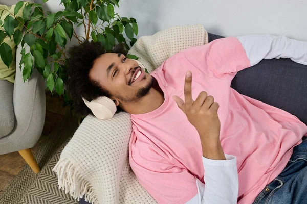 Genç, yakışıklı bir adam kanepede uzanıyor, gülümsüyor ve bitkilerle çevrili müzik dinliyor..