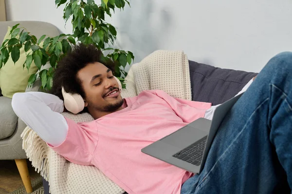 Gülümseyen genç adam rahat bir kanepeye uzanıp dizüstü bilgisayarında bir şey izliyor..