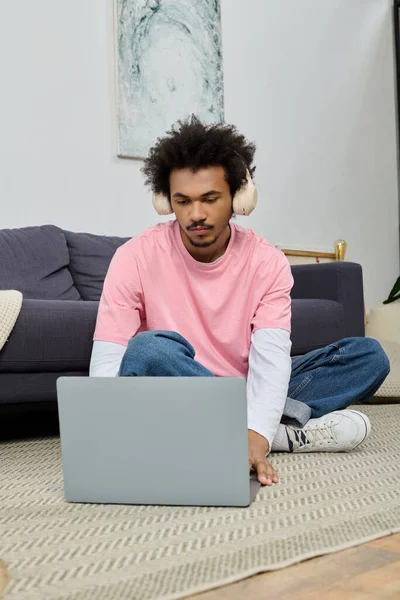 Kulaklıklı genç adam rahat bir yerde dinlenirken dizüstü bilgisayara odaklanmış..