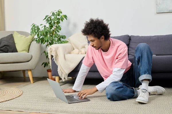 Odaklanmış genç bir adam halıya oturmuş, parlak, davetkar bir oturma odasında dizüstü bilgisayarla çalışıyor..