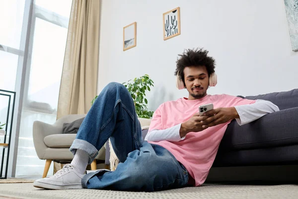 Yakışıklı bir genç adam yerde rahat bir şekilde uzanıyor, telefonu ve müziğine dalmış..