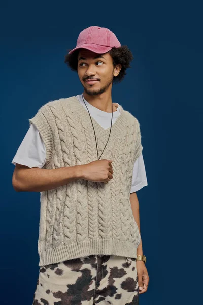 Genç yakışıklı bir adam modaya uygun örgü bir yelek sergiliyor. Şapkayla eşleştirilmiş, zahmetsiz bir cazibesi var..