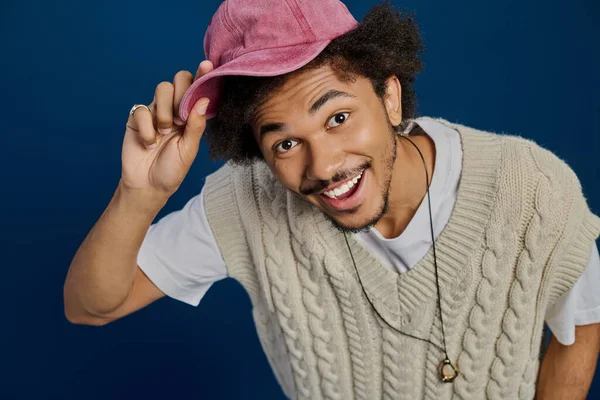 Yakışıklı genç adam pembe şapkasını renkli bir arka planda gezdirirken mutluluğunu ifade eder..