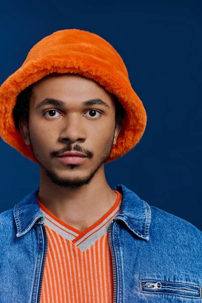 Turuncu şapkalı ve kot ceketli yakışıklı genç adam doğrudan bakıyor, büyüleyici ve tarz sahibi..