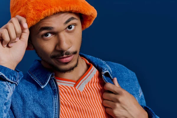 Parlak turuncu şapkalı ve kot ceketli adam ışıl ışıl gülümserken cazibesini ve kişiliğini gösteriyor..