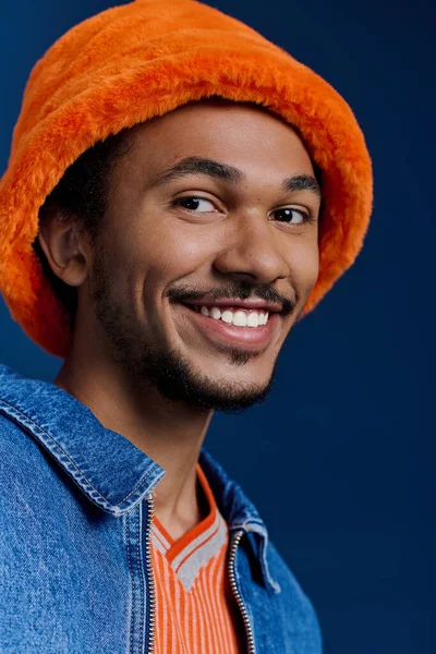 Çekici bir genç adam pofuduk turuncu bir şapka ve kot ceket giyer, mutluluk ve tarz saçar..